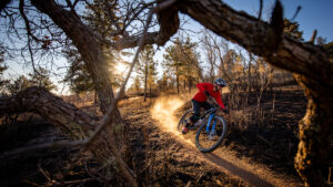 Mountain biker riding a dusty trail with the setting sun beaming behind him.