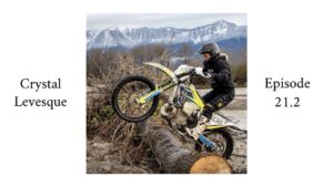 Woman enduro rider riding over a log with mountains in the background.
