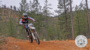 Dirt bike rider riding on red clay through the trees.