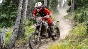 Dirt bike racer riding down the trail and hanging off the bike.