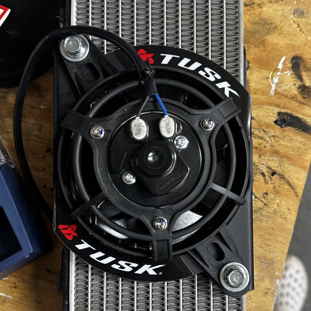 Tusk radiator fan installed on a GASGAS dirt bike, showing wiring and radiator detail on a workbench.